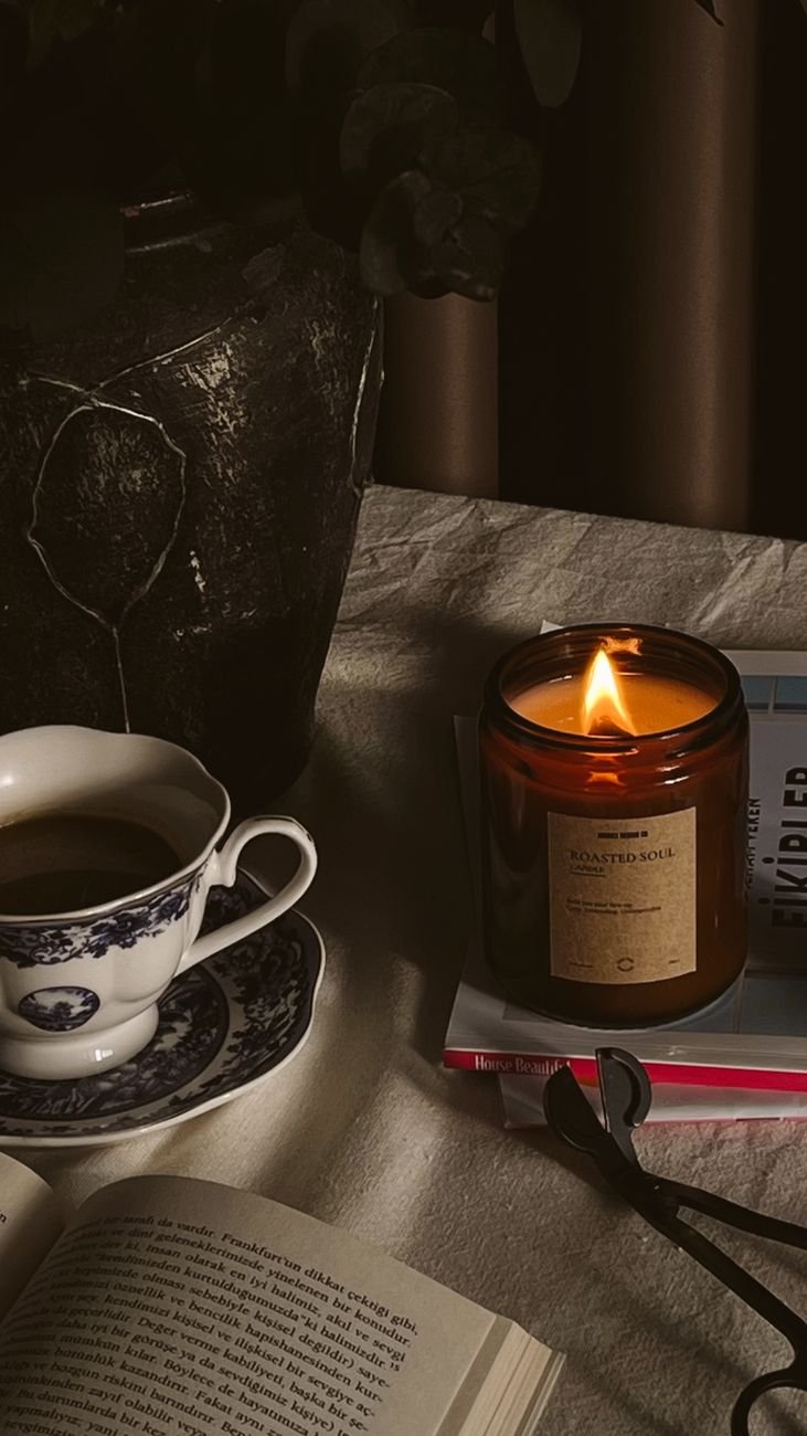 A lit candle on an evening table beside coffee and books.