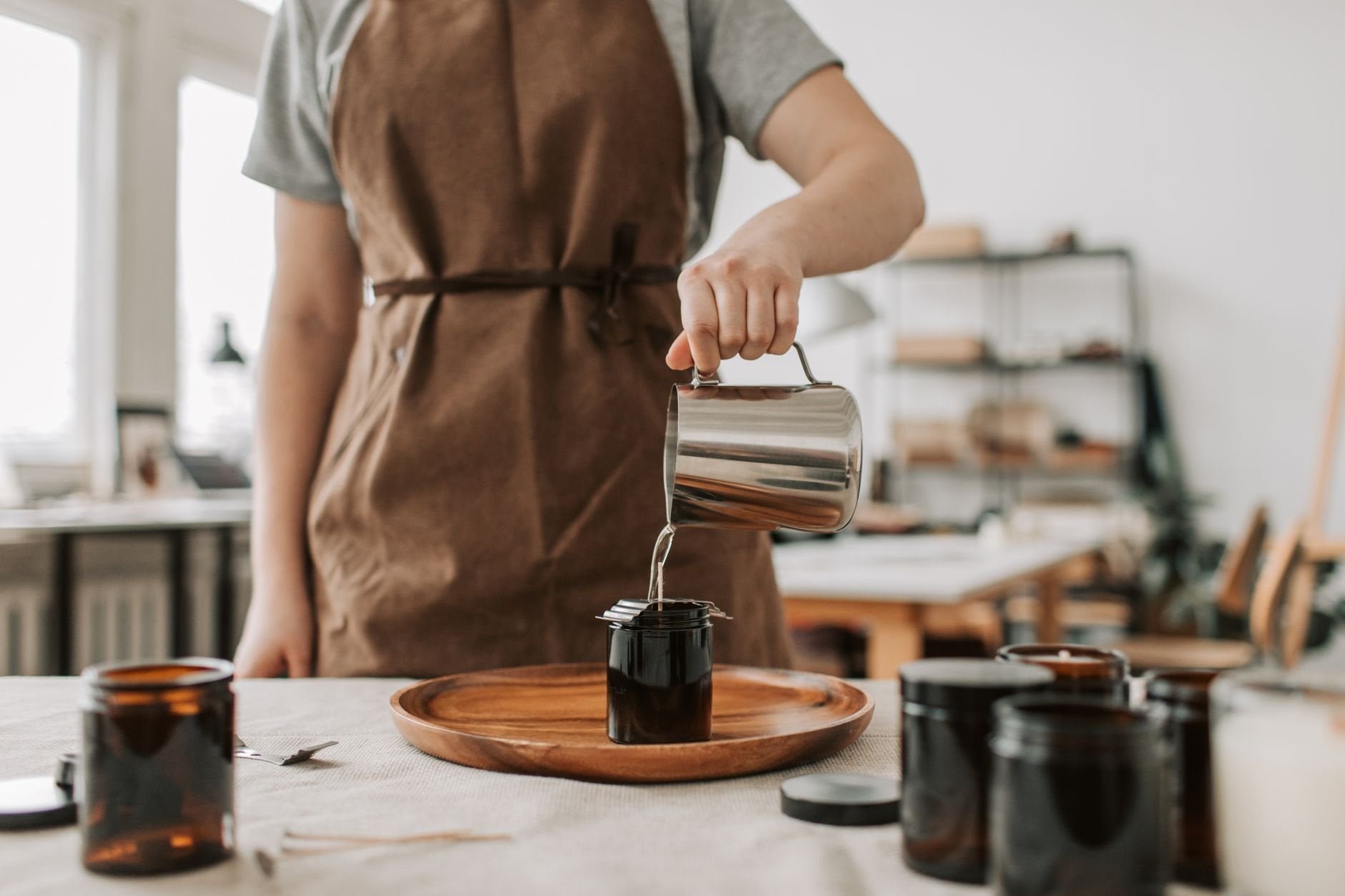 A maker pouring wax into glass jars in a workshop.